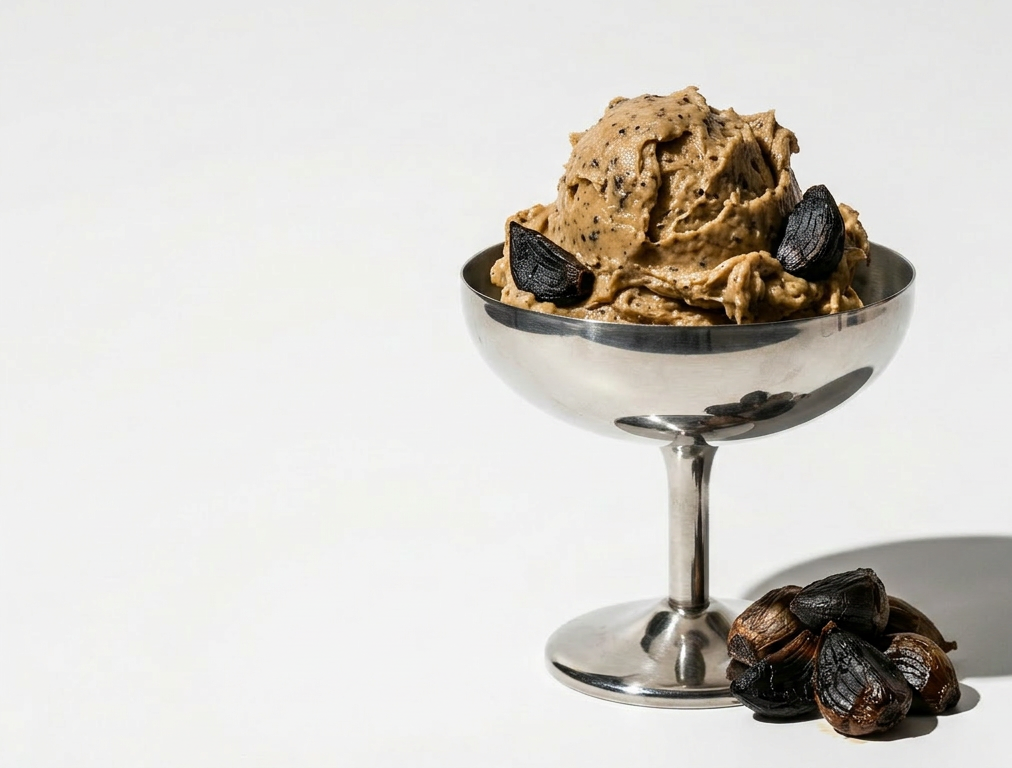 Black garlic cultured butter in a silver coupe glass with whole black garlic cloves around for garnish and styling